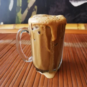 Hainan cham with sweet milk tea topped with thick creamy foam overflowing from clear glass mug
