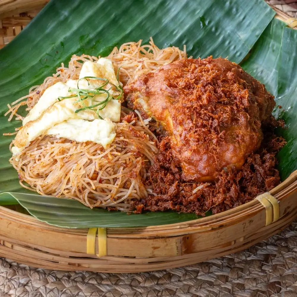 Mee siam ayam pop with crispy fried chicken, rice vermicelli, and fried egg thinly sliced served on banana leaf