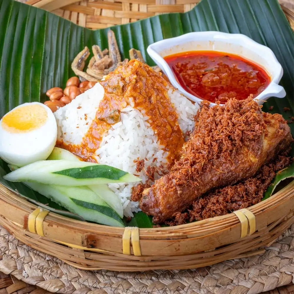 Nasi lemak ayam pop with coconut rice, crispy fried chicken, boiled egg, and fried anchovies on banana leaf