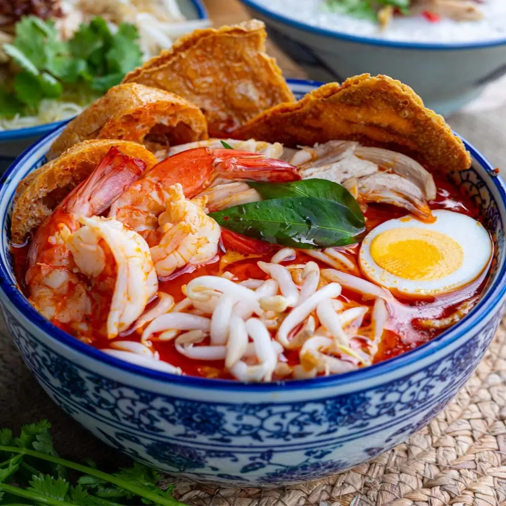 Singapore laksa with prawns, rice noodles, hard-boiled egg, and coconut curry broth in traditional blue bowl.
