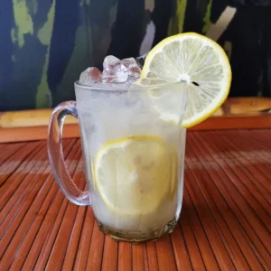 Lemon barley with refreshing citrus drink, barley, ice cubes, and fresh lemon slice garnish in clear glass mug